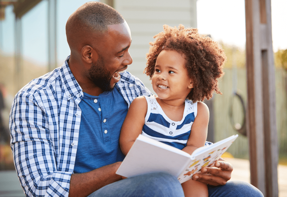 A man and child reading a book outside.